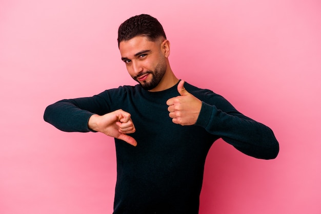 Young mixed race man isolated on pink wall showing thumbs up and thumbs down, difficult choose concept