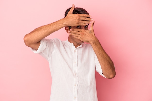 Photo young mixed race man isolated on white background blink at the camera through fingers, embarrassed covering face.