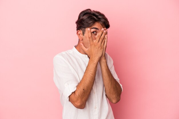 Photo young mixed race man isolated on white background blink through fingers frightened and nervous.