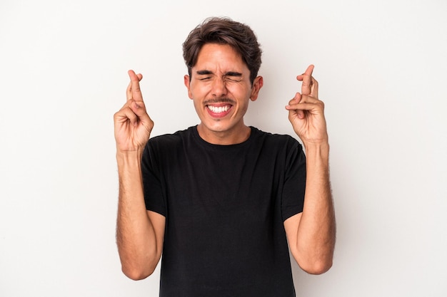 Young mixed race man isolated on white background crossing fingers for having luck