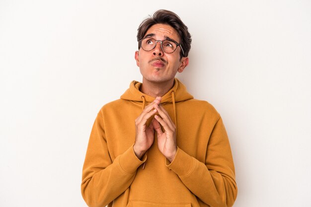 Young mixed race man isolated on white background holding hands in pray near mouth, feels confident.