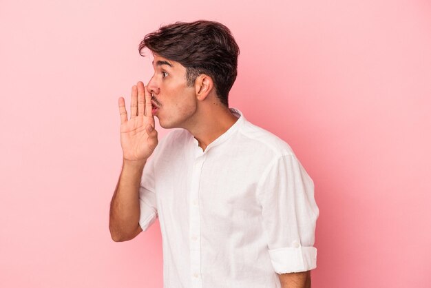 Young mixed race man isolated on white background is saying a secret hot braking news and looking aside