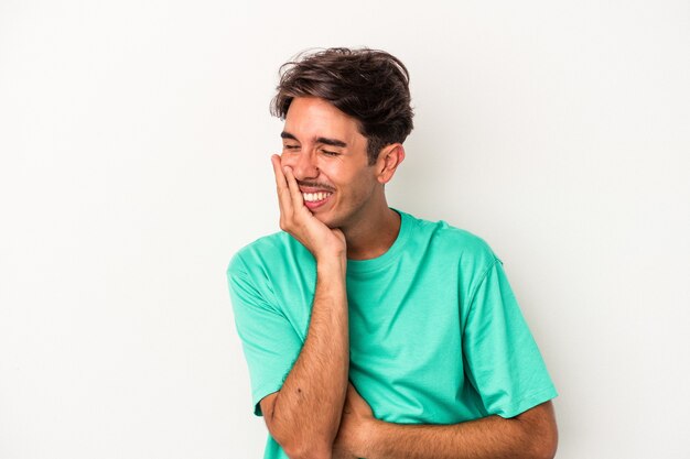 Young mixed race man isolated on white background laughs happily and has fun keeping hands on stomach.