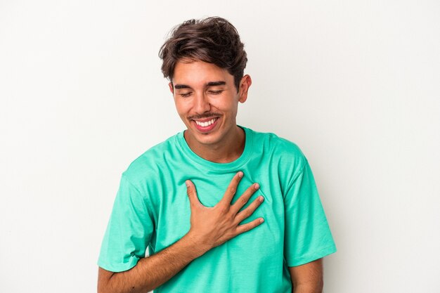 Young mixed race man isolated on white background laughs out loudly keeping hand on chest.