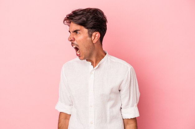 Young mixed race man isolated on white background shouting very angry, rage concept, frustrated.