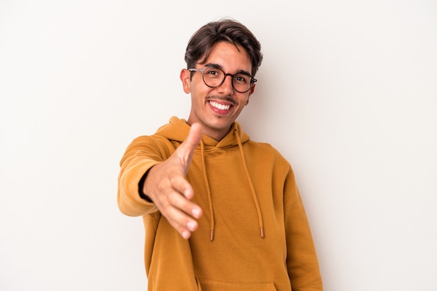 Young mixed race man isolated on white background stretching hand at camera in greeting gesture.