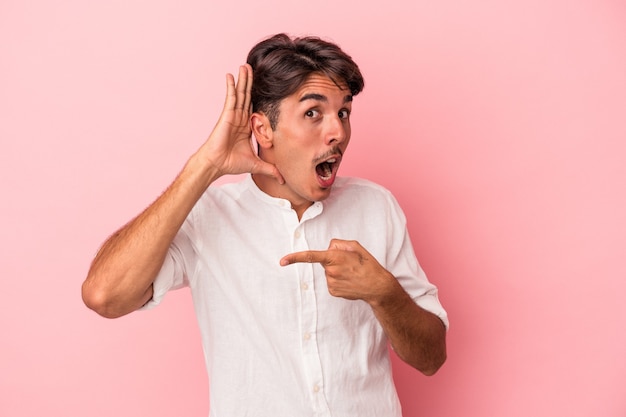 Young mixed race man isolated on white background trying to listening a gossip.