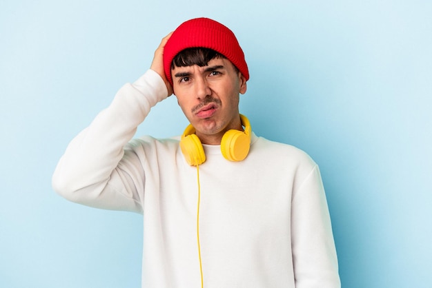 Young mixed race man listening to music isolated on blue background being shocked, she has remembered important meeting.