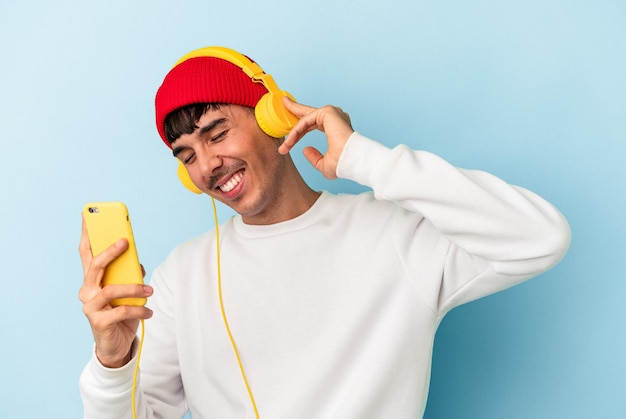 Young mixed race man listening to music isolated on blue background