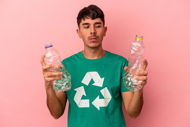 Young mixed race man recycled plastic isolated on pink background