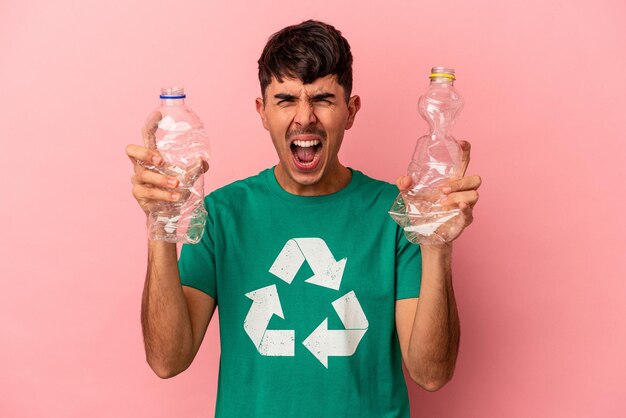 Young mixed race man recycled plastic isolated on pink background