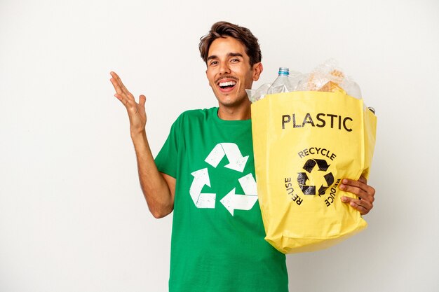 Young mixed race man recycling plastic isolated on yellow background receiving a pleasant surprise, excited and raising hands.