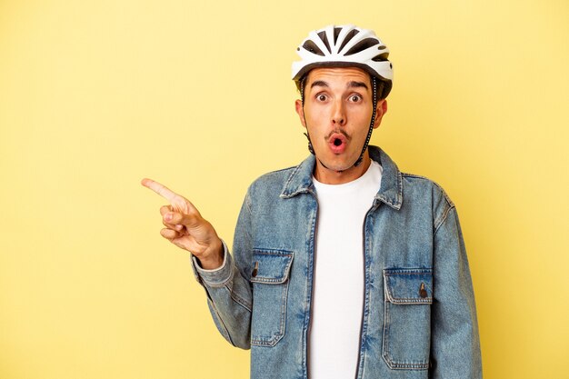 Young mixed race man wearing a helmet bike isolated on yellow background pointing to the side