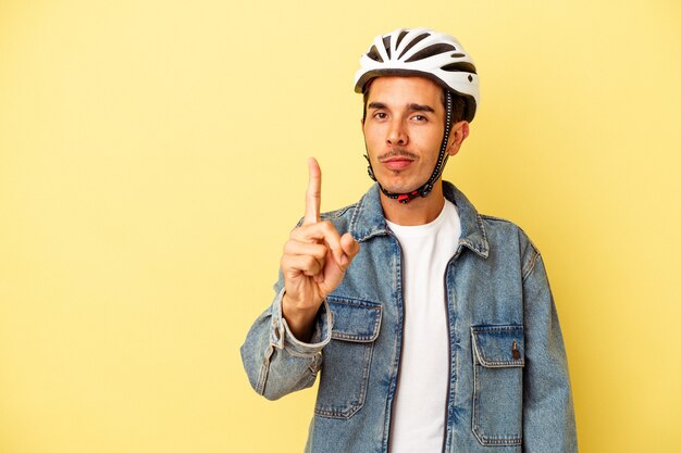 Young mixed race man wearing a helmet bike isolated on yellow background showing number one with finger.