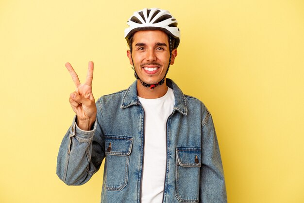 Young mixed race man wearing a helmet bike isolated on yellow background showing number two with fingers.