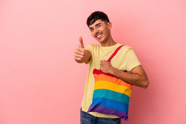 Young mixed race man wearing LGTB bag isolated on pink background