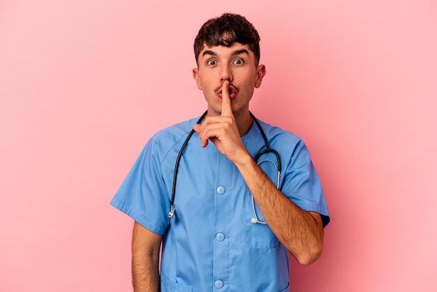 Young mixed race nurse man isolated on pink background keeping a secret or asking for silence.