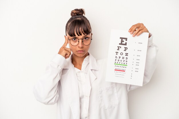 Young mixed race optician woman doing a test isolated on white background  pointing temple with finger, thinking, focused on a task.