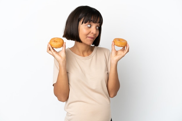 Young mixed race pregnant woman isolated on white background holding donuts