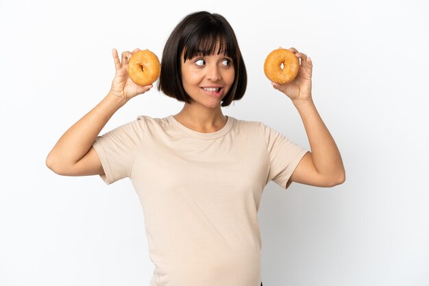 Young mixed race pregnant woman isolated on white background holding donuts