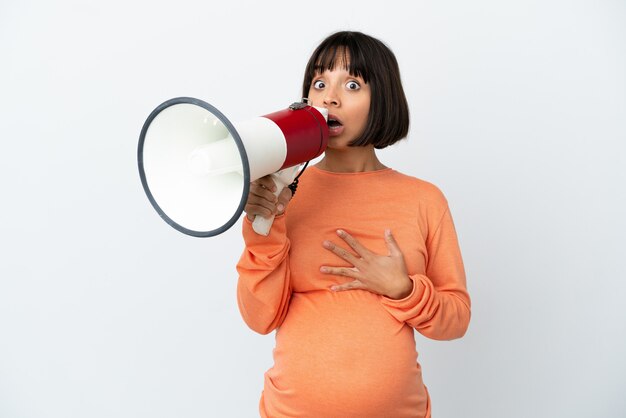 Young mixed race pregnant woman isolated on white background shouting through a megaphone with surprised expression