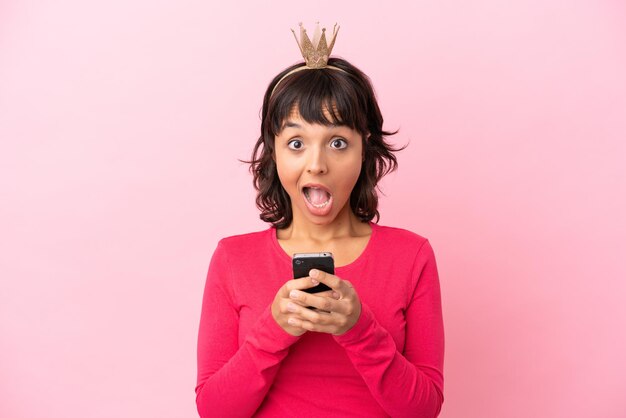 Photo young mixed race princess with crown isolated on pink background surprised and sending a message