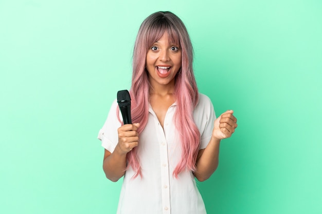 Giovane donna cantante di razza mista con i capelli rosa isolata su sfondo verde che celebra una vittoria nella posizione del vincitore