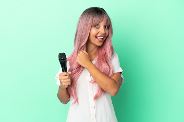 Young mixed race singer woman with pink hair isolated on green background celebrating a victory