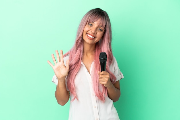 Young mixed race singer woman with pink hair isolated on green background counting five with fingers