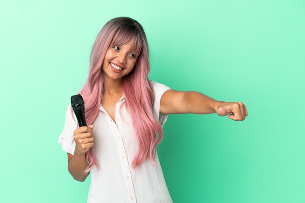 親指を立てるジェスチャーを与える緑の背景に分離されたピンクの髪を持つ若い混血歌手の女性