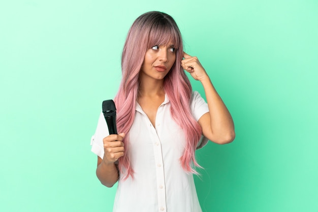 Young mixed race singer woman with pink hair isolated on green background having doubts and thinking