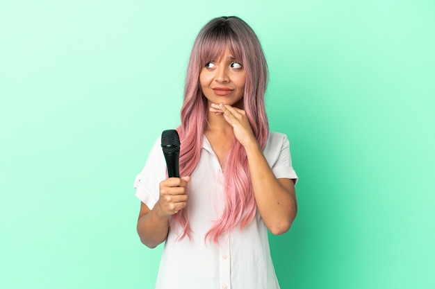 Young mixed race singer woman with pink hair isolated on green background having doubts