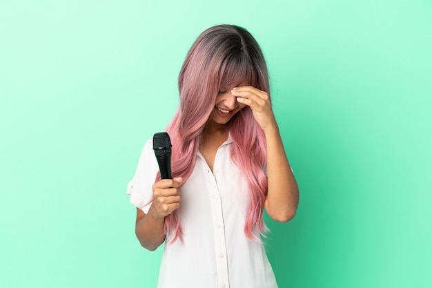 Young mixed race singer woman with pink hair isolated on green background laughing