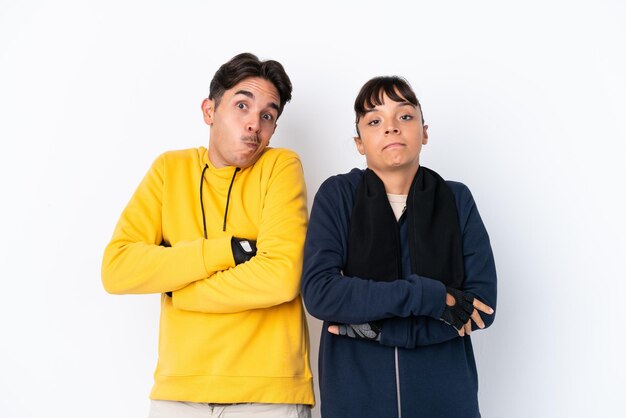 Young mixed race sport couple isolated on white background making doubts gesture while lifting the shoulders