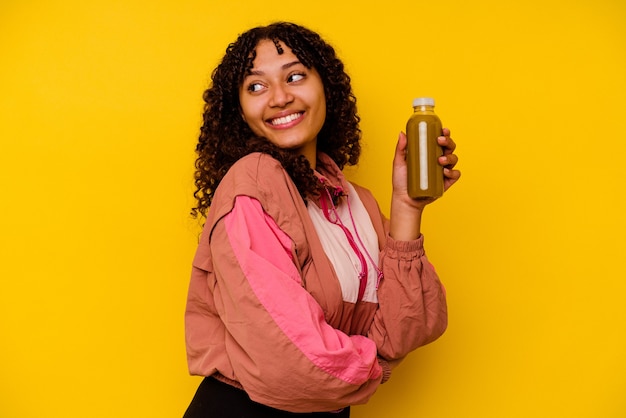 Young mixed race sport woman holding a smoothie isolated on yellow