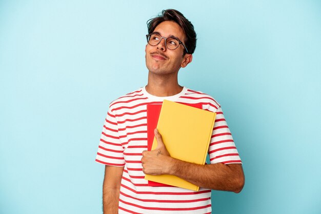 Young mixed race student man holding books isolated on blue background dreaming of achieving goals and purposes