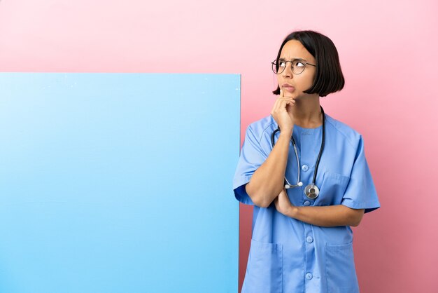 Young mixed race surgeon woman with a big banner over isolated background having doubts and thinking