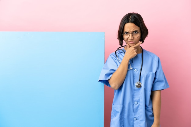 Young mixed race surgeon woman with a big banner isolated background having doubts