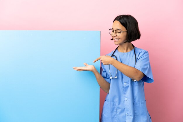 Young mixed race surgeon woman with a big banner over isolated background holding copyspace imaginary on the palm to insert an ad