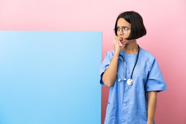 Photo young mixed race surgeon woman with a big banner over isolated background is a little bit nervous