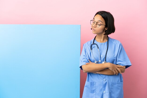 Young mixed race surgeon woman with a big banner isolated background and looking up