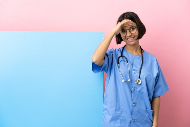 Young mixed race surgeon woman with a big banner over isolated background saluting with hand with happy expression