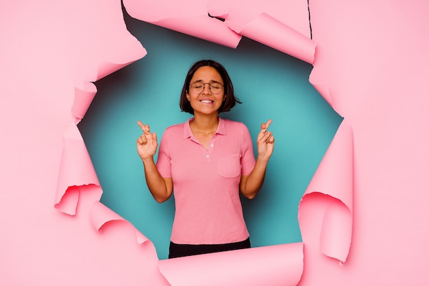 Young mixed race woman behind a broken background doubting and shrugging shoulders in questioning gesture.