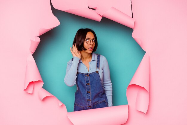 Young mixed race woman behind a broken background has friendly expression, pressing palm to chest. Love concept.