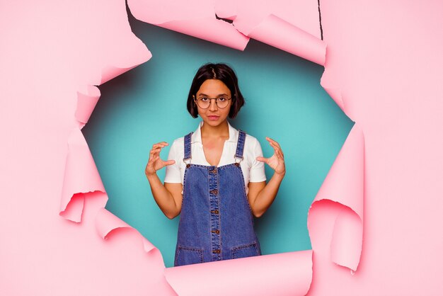 Young mixed race woman behind a broken background looking sideways with doubtful and skeptical expression.