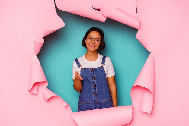 Young mixed race woman behind a broken background smiling and showing a heart shape with hands.