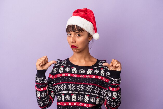 紫色の背景に分離されたクリスマスを祝う若い混血の女性は、誇りと自信を持って、従うべき例を感じます。