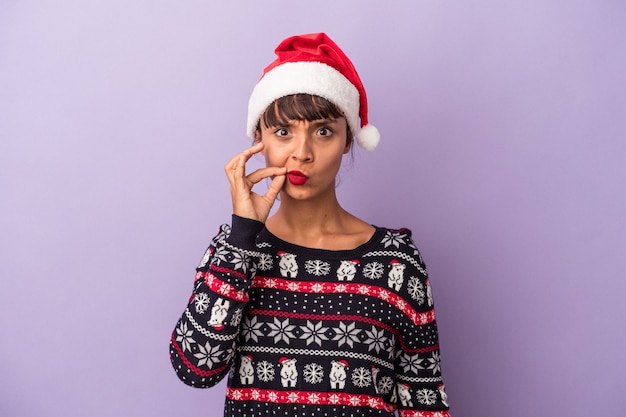 Giovane donna di razza mista che celebra il natale isolato su sfondo viola con le dita sulle labbra mantenendo un segreto.