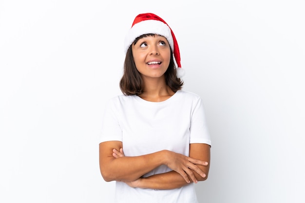Молодая женщина смешанной расы празднует Рождество изолированно на белом фоне, глядя вверх, улыбаясь
