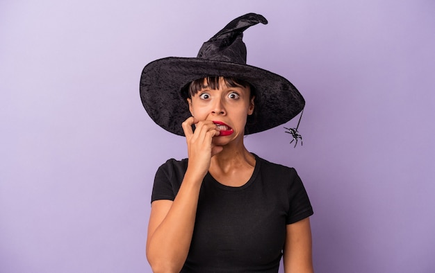 Young mixed race woman disguised as a witch isolated on purple background  biting fingernails, nervous and very anxious.